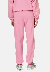Jogging en polaire rose avec une coupe fuselée, taille élastique et chevilles resserrées, assortis à des chaussures de sport grises et des chaussettes roses.