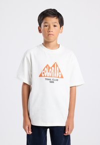 Valkoinen puuvillainen t-paita, jossa on oranssi vuoristokuvasto ja tekstit "COLORADO" ja "TRAIL CLUB 1989". Lyhyet hihat, rento leikkaus.