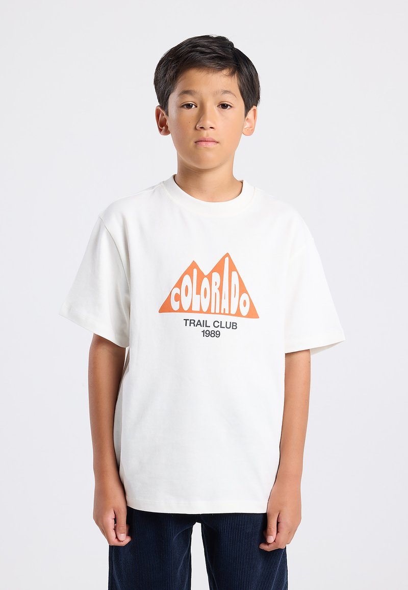Valkoinen puuvillainen t-paita, jossa on oranssi vuoristokuvasto ja tekstit "COLORADO" ja "TRAIL CLUB 1989". Lyhyet hihat, rento leikkaus.