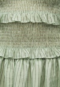 Ανοιχτό πράσινο ύφασμα με κατακόρυφες μαύρες ρίγες, με πιετά με ελαστικό και στρωματοποιημένες λεπτομέρειες βολάν.