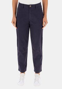 Pantaloni di cotone blu navy con gamba affusolata, chiusura con bottone, tasche frontali e una texture liscia, abbinati a sneaker bianche.