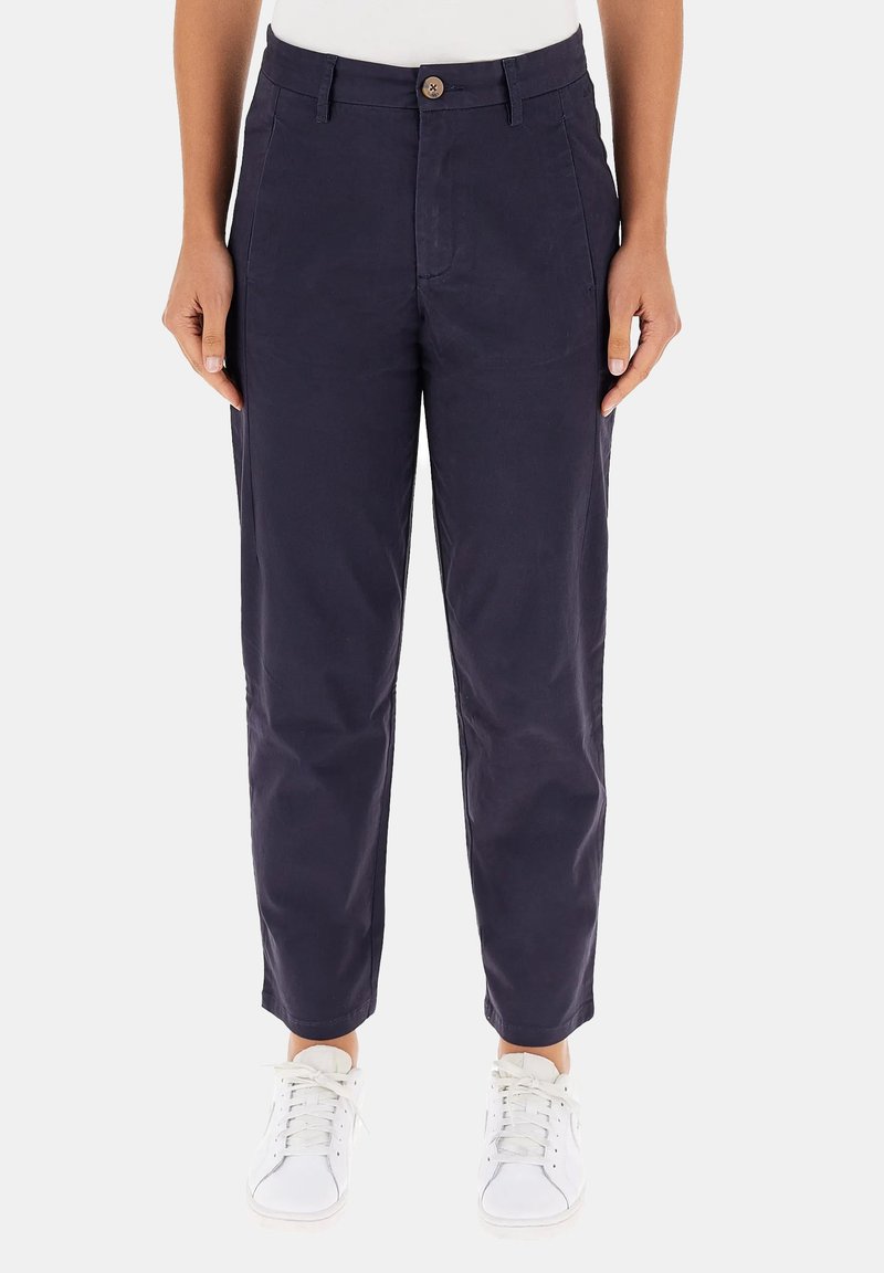 Pantaloni di cotone blu navy con gamba affusolata, chiusura con bottone, tasche frontali e una texture liscia, abbinati a sneaker bianche.