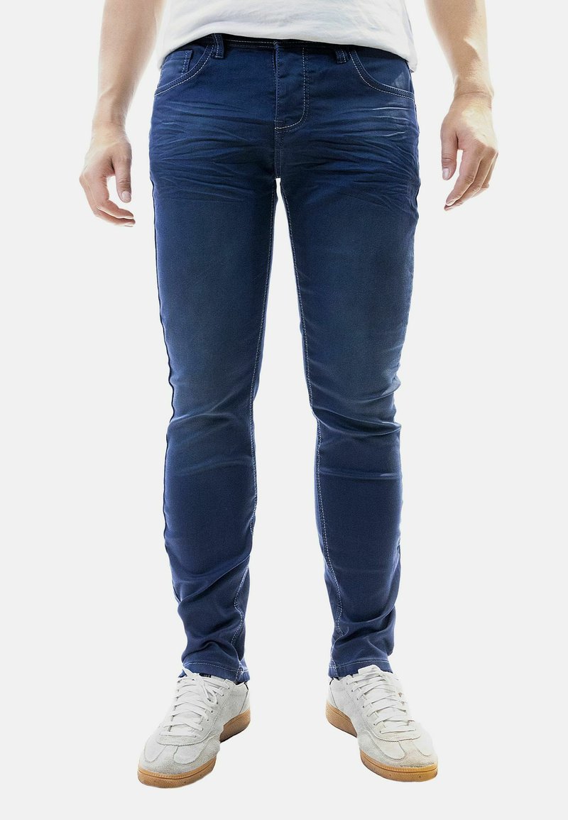 Blaue Denim-J Jeans mit einem schlanken Schnitt, die subtile Verwaschungen und gestickte Details aufweisen. Kombiniert mit weißen Sportschuhen.