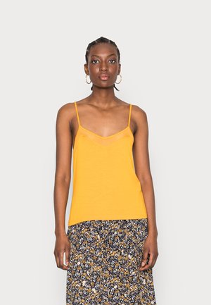 Top amarelo sem mangas com decote em V e sobreposição translúcida. Tecido suave, corte solto. Combinado com uma saia com padrão floral em tons escuros.