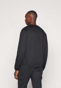 Svart sweatshirt med långa ärmar, rund hals och elastiska muddar. Slät textur och minimalistisk design. Kombinerad med matchande svarta byxor.