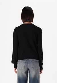 Suéter negro de punto con mangas largas, cuello redondo y sutil detalle abullonado en los hombros, combinado con unos vaqueros de cintura alta en azul claro.