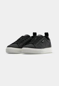 Μαύρα αθλητικά παπούτσια με λείο συνθετικό επάνω μέρος, λευκή ελαστική σόλα, στρογγυλεμένη μύτη, επίπεδα κορδόνια και θηλιές έλξης στη φτέρνα.