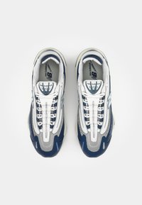 Pár bílých a námořnických běžeckých bot New Balance 1000 pohledem shora na čistém bílém pozadí.