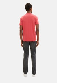 Koralfarbenes Baumwoll-T-Shirt mit kurzen Ärmeln, Rundhalsausschnitt, getragen mit dunkelgrauen Jeans und weißen Sneakers. Sichtbare Nähte und lässiger Schnitt.