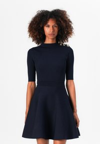 Abito in maglia blu navy con top a costine, collo alto, maniche corte e gonna svasata, arricchito da bottoni dorati sulla spalla.