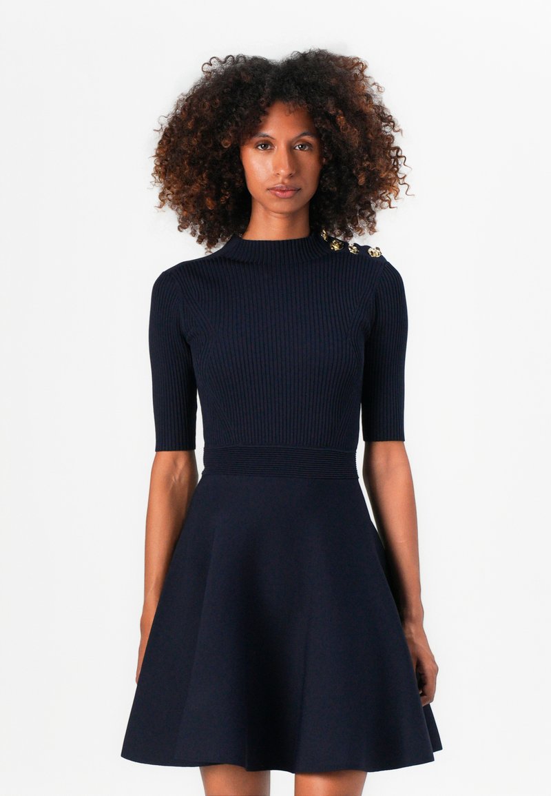 Abito in maglia blu navy con top a costine, collo alto, maniche corte e gonna svasata, arricchito da bottoni dorati sulla spalla.