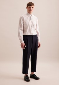 Camicia a quadri rosa chiaro e bianca con colletto standard, abbinata a pantaloni sartoriali blu scuro e scarpe nere. Design minimalista.