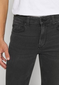 Černé džíny z denimu s úzkým střihem, které mají pět kapes, zapínání na knoflík a zip a jemně vybledlou texturu látky.