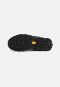Suola di scarpa in gomma nera con profonde scanalature per il grip e un logo giallo prominente. Superficie testurizzata progettata per la presa e la durata.