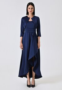 Vestito lungo blu navy con corpetto aderente, maniche a tre quarti e un accento floreale in vita. Presenta un orlo asimmetrico.