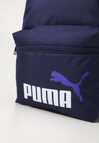 Marine ryggsekk laget av slitesterk stoff, med en frontlomme med glidelås og en fremtredende hvit "PUMA"-logo med et lilla hoppende kattedesign.