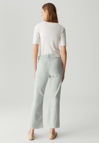 Jeans a zampa di elefante verde chiaro con una texture in tweed, tasche posteriori e vita alta. Abbinate a una T-shirt bianca aderente e a delle scarpe beige senza lacci.