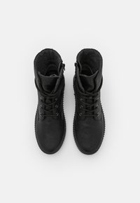 Bottines noires avec une surface extérieure texturée et imperméable, embout surélevé, lacets à l'avant et doublure intérieure en polaire douce. Fermeture éclair sur le côté.