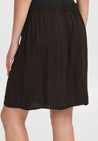 Gonna marrone scuro, lunghezza al ginocchio, con finitura texture, vita elastica e vestibilità rilassata. Presenta uno spacco laterale per facilitare i movimenti.