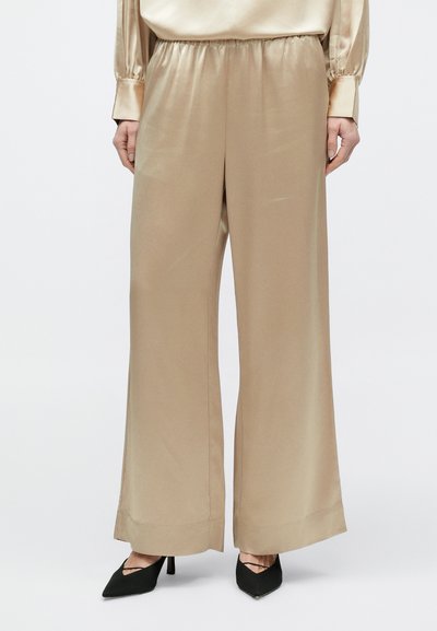 Bézs szatén, bő szárú nadrág, hozzávaló szatén blúzzal és fekete, vékony pántos, hegyes orrú magassarkúval viselve.