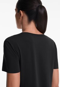Black short-sleeve shirt made from smooth fabric. Features a round neckline and perforated detail at the upper back for breathability.