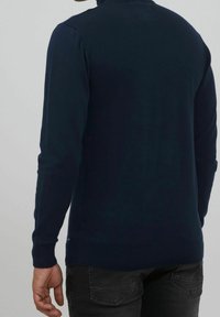 Granatowy sweter dzianinowy z wysokim kołnierzem, długimi rękawami i dopasowanym dołem. Teksturowany materiał z gładkim wykończeniem.