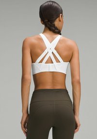 Sujetador deportivo blanco con tirantes cruzados y textura suave. Combinado con leggings de talle alto en verde oliva, mostrando un diseño ajustado.