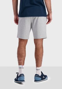 Šedé sportovní šortky vyrobené z měkké tkaniny, s elastickým pasem. Nosené s námořnickými teniskami a bílými ponožkami s logem.