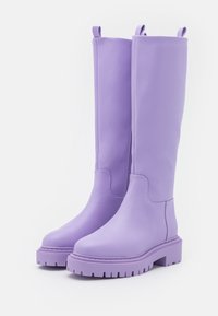 Bottes violettes montant jusqu'au genou avec une texture lisse, une semelle épaisse et des languettes de traction. Présentent un bout arrondi et des détails de couture minimalistes.