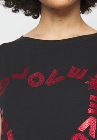 Černé tričko s velkým červeným glitrovým nápisem "LOVE", kulatým výstřihem a krátkým rukávem.