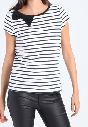 Stripet kortærmet top i hvid og marineblå, med en bueaccent nær halsen og en afslappet pasform. Sammen med sorte bukser.