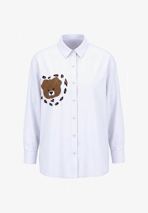 Hvid langærmet skjorte med knapper og et teddybjørneansigt broderet på brystet, omgivet af leopardpletter.