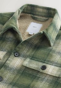 Zaļš un bēšs šaha raksts flaneles krekls ar mīkstu krējuma vilnas oderi, ar diviem melniem pogām un kabatu. Uzlīme redzama iekšpusē.