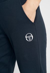 Navyblauwe katoenen joggingbroek met een gladde textuur, met een zijzak en een wit geborduurd logo op de bovenbeen.