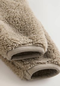 Tissu beige et moelleux avec une surface texturée. Comprend des manches douces et pelucheuses ainsi que des bords de poignets lisses et contrastants.