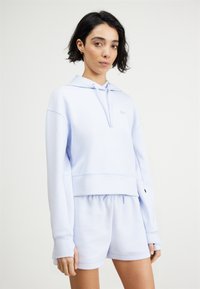 Hanorac de culoare albastru deschis și pantaloni scurți asortați, confecționați dintr-o țesătură moale. Hanoracul are șnur și manșete cu nervuri; pantaloni scurți au talie elastică.