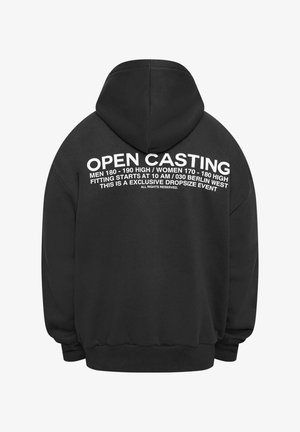 Juoda kapucė su baltais užrašais nugarinėje pusėje, featuring frazę "ATVIRO JUDĖJIMO KASTINGAS" ir dydžių vedlė vyrams ir moterims.