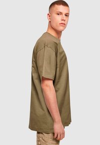 Olive green cotton t-shirt with short sleeves, a crew neckline, and a relaxed fit, featuring a subtle logo detail on the side.