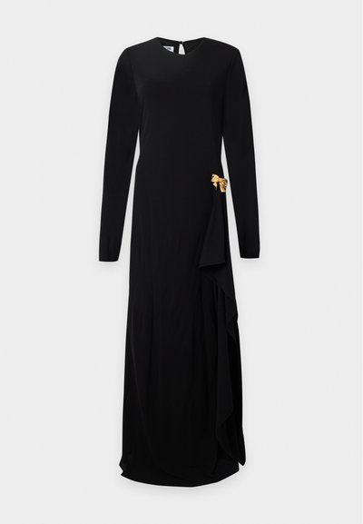 Longue robe noire à manches longues, encolure ronde, avec un détail nœud doré sur la hanche droite avec tissu drapé.
