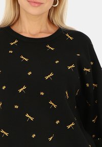 Czarny sweter z okrągłym dekoltem, zdobiony złotymi haftowanymi ważkami i pszczołami w rozproszonym wzorze. Wykonany z miękkiego materiału.