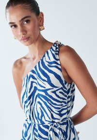 Haljina s jednom naramenicom u laganoj tkanini s plavo-bijelim uzorkom zebre, detaljem vezanja u struku i ukrasnim metalnim elementom na naramenici.