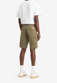 Shorts kaki à coupe droite, deux poches arrière et une étiquette. Portés avec un t-shirt blanc et des chaussettes blanches, associés à des baskets.