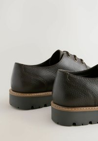 Sorte lædersko med en struktureret overflade, rund tå, sort gummisål og brun syning langs kanten. Design med tre snørehuller.