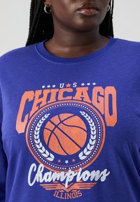 Μπλε μακρυμάνικο μπλούζα με λογότυπο "Πρωταθλητές Η.Π.Α. Σικάγο" σε πορτοκαλί και λευκό, με γραφικό μπάσκετ και δάφνινα κλαδιά.