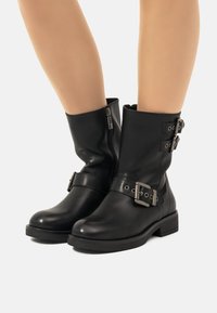 Stivali alla caviglia in pelle nera con punta rotonda, dotati di cinghie regolabili con accessori in argento e zip laterale per una facile calzata.
