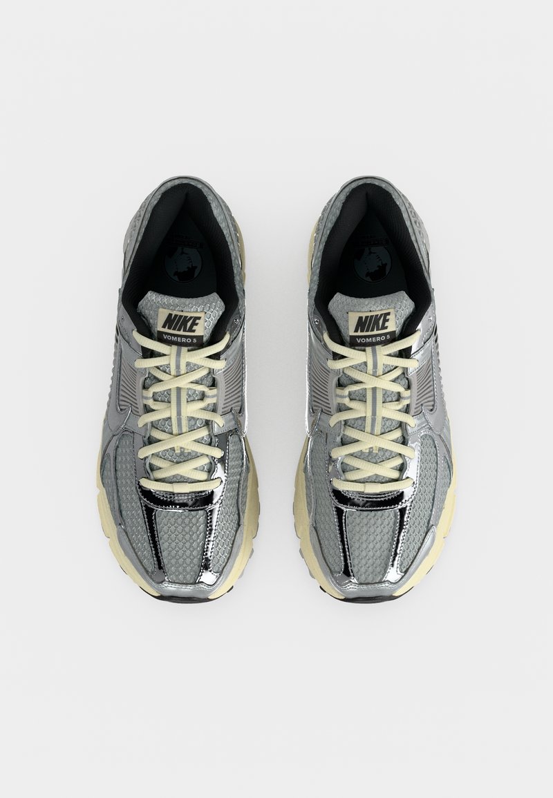 Zapatillas de running Nike Vomero 5 grises con cordones crema y suelas beige gruesas, vistas desde arriba sobre un fondo blanco.