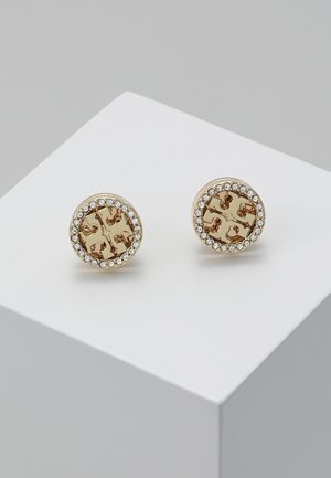Boucles d'oreilles clous rondes en or avec un motif de croix découpé, bordées d'un cercle de petits cristaux clairs sur une surface blanche.