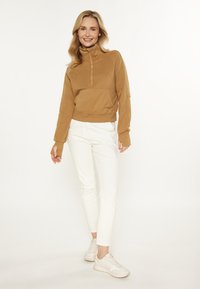 Pullover mezza zip in pile beige con tasca a marsupio, abbinato a pantaloni bianchi slim-fit e sneakers chiare. Texture liscia con polsini a costine.