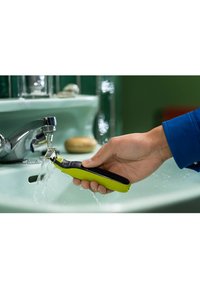 Rasoi elettrico portatile con un corpo nero e verde brillante e strutturato, tenuto sotto acqua corrente in un lavello del bagno.