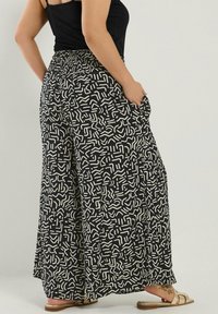 Svarta vida byxor med ett krämfärgat abstrakt mönster, elastisk midja, sidofickor och lättviktsmaterial. Avslappnad design som passar för varmt väder.